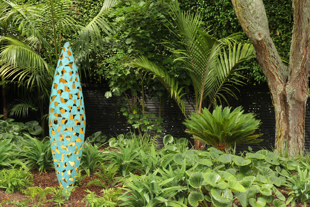 Layered planting design with Ligularia, Nikau, and garden sculpture